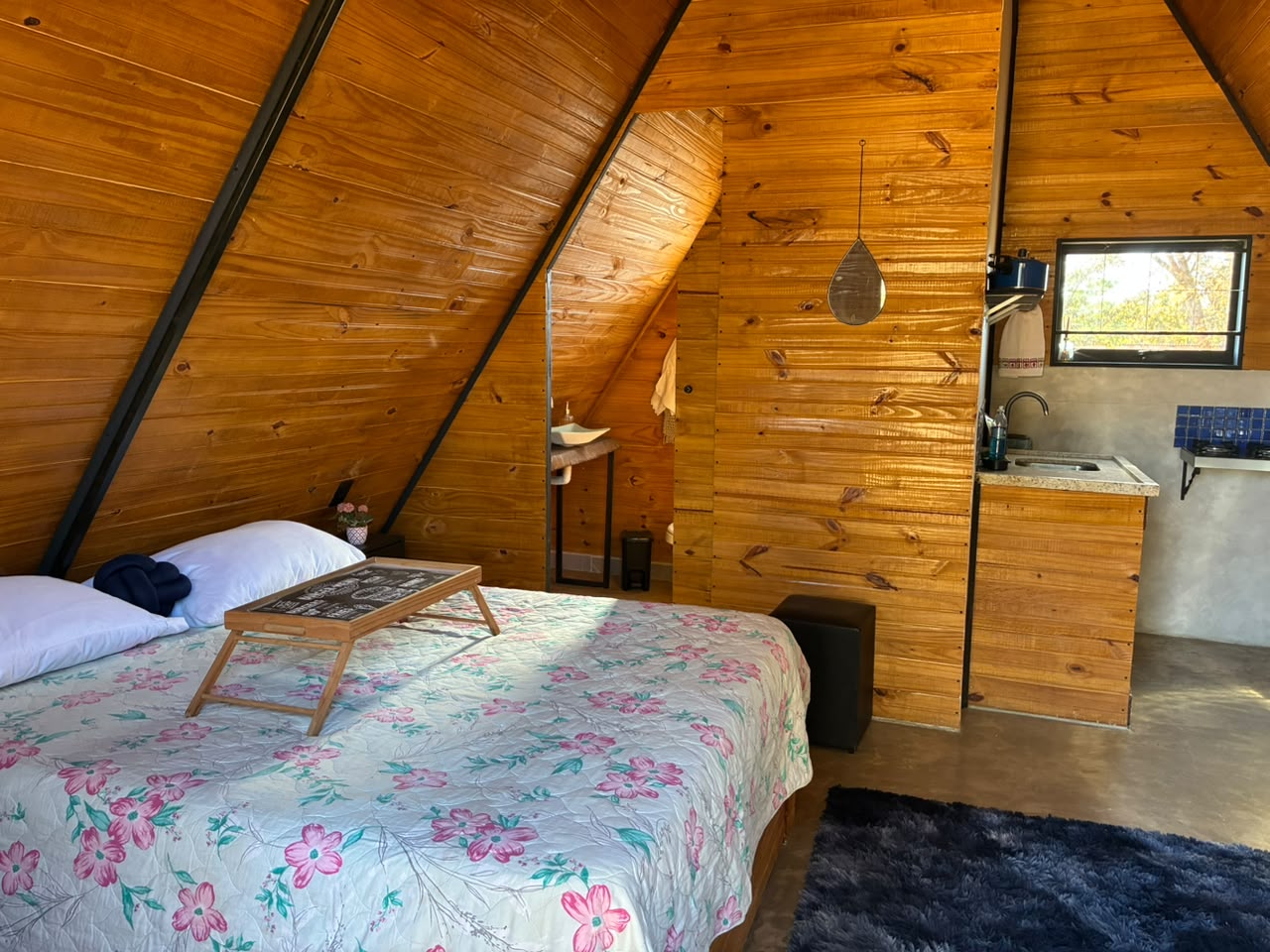 Interior do chalé de madeira imerso na natureza, com cama, cozinha compacta e banheiro