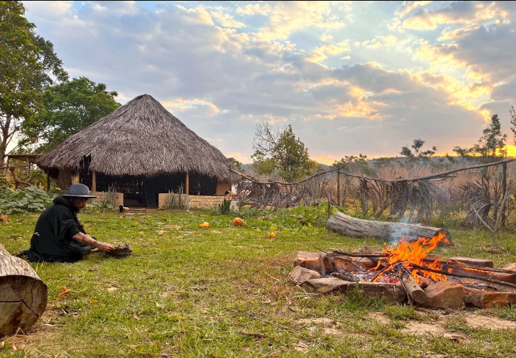 O espaço do retiro: fogueira acesa, kupixawa, oca, cabana e as montanhas da Chapada ao entardecer