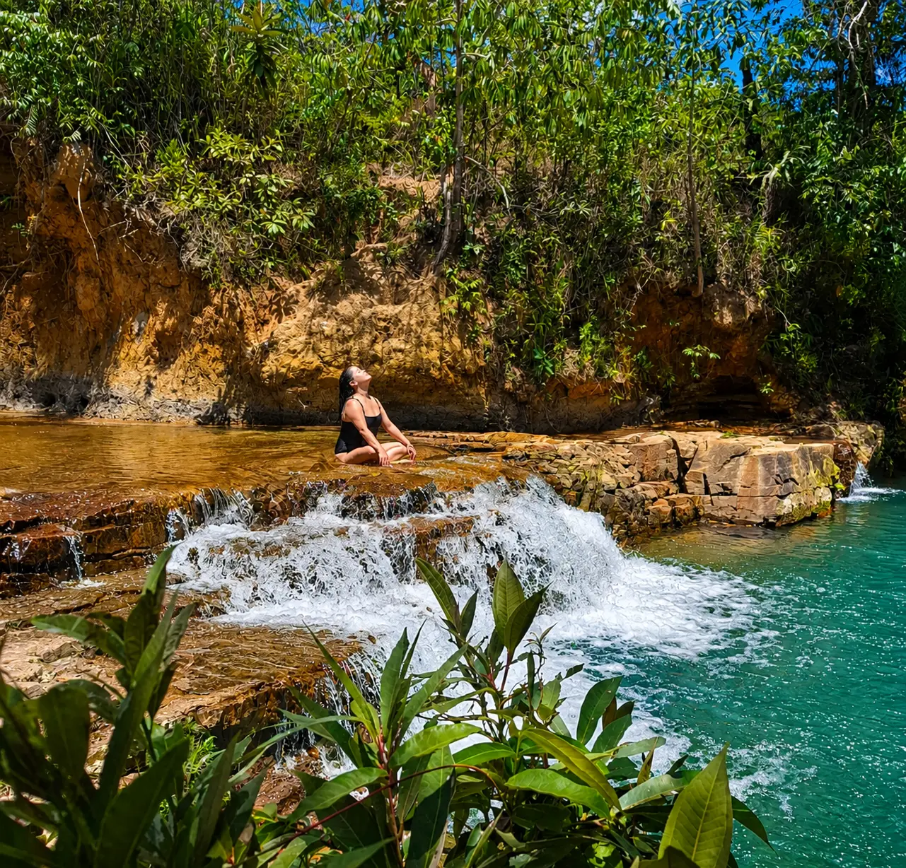 Mulher meditando sobre as pedras de uma cachoeira de águas turquesa