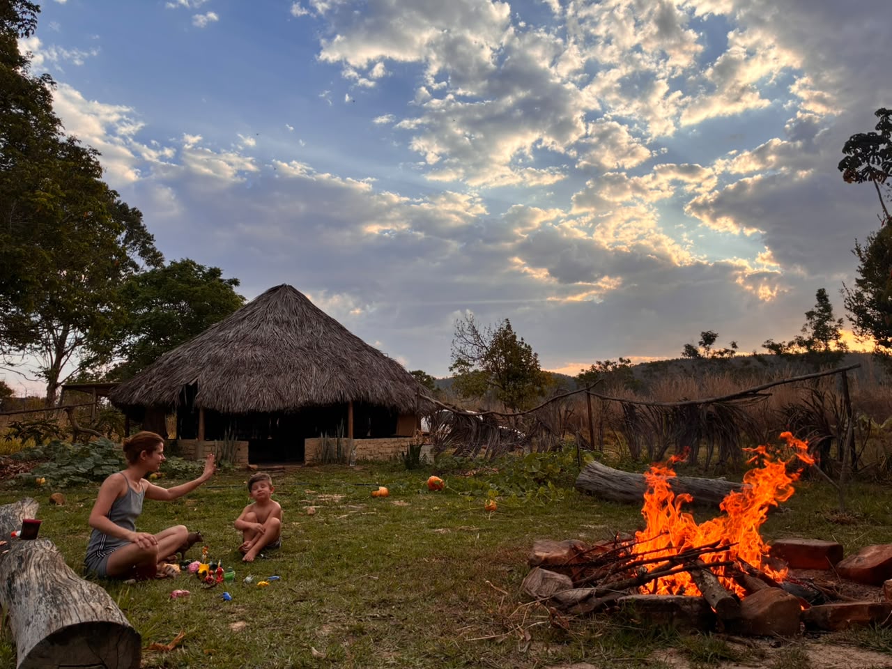 Oca de palha, fogueira e o céu do Cerrado no fim da tarde