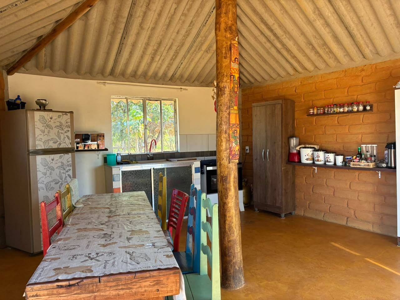 Cozinha comunitária de tijolo e madeira com mesa longa e cadeiras coloridas